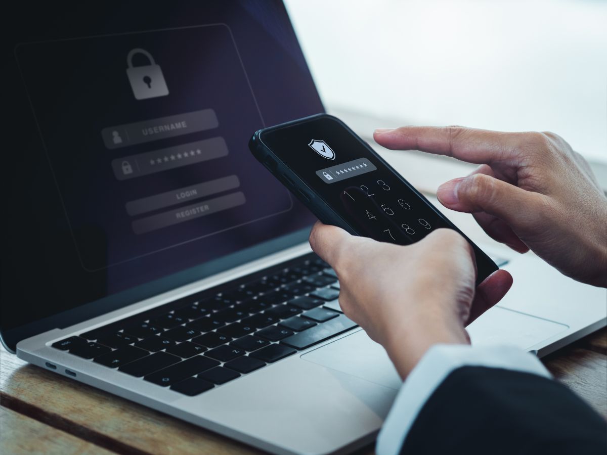 Concetto di autenticazione in due passaggi (2FA). Icona scudo e codice password visualizzati sullo schermo dello smartphone mentre l'uomo d'affari accede al computer portatile, verifica dell'identità, tecnologia di sicurezza informatica.